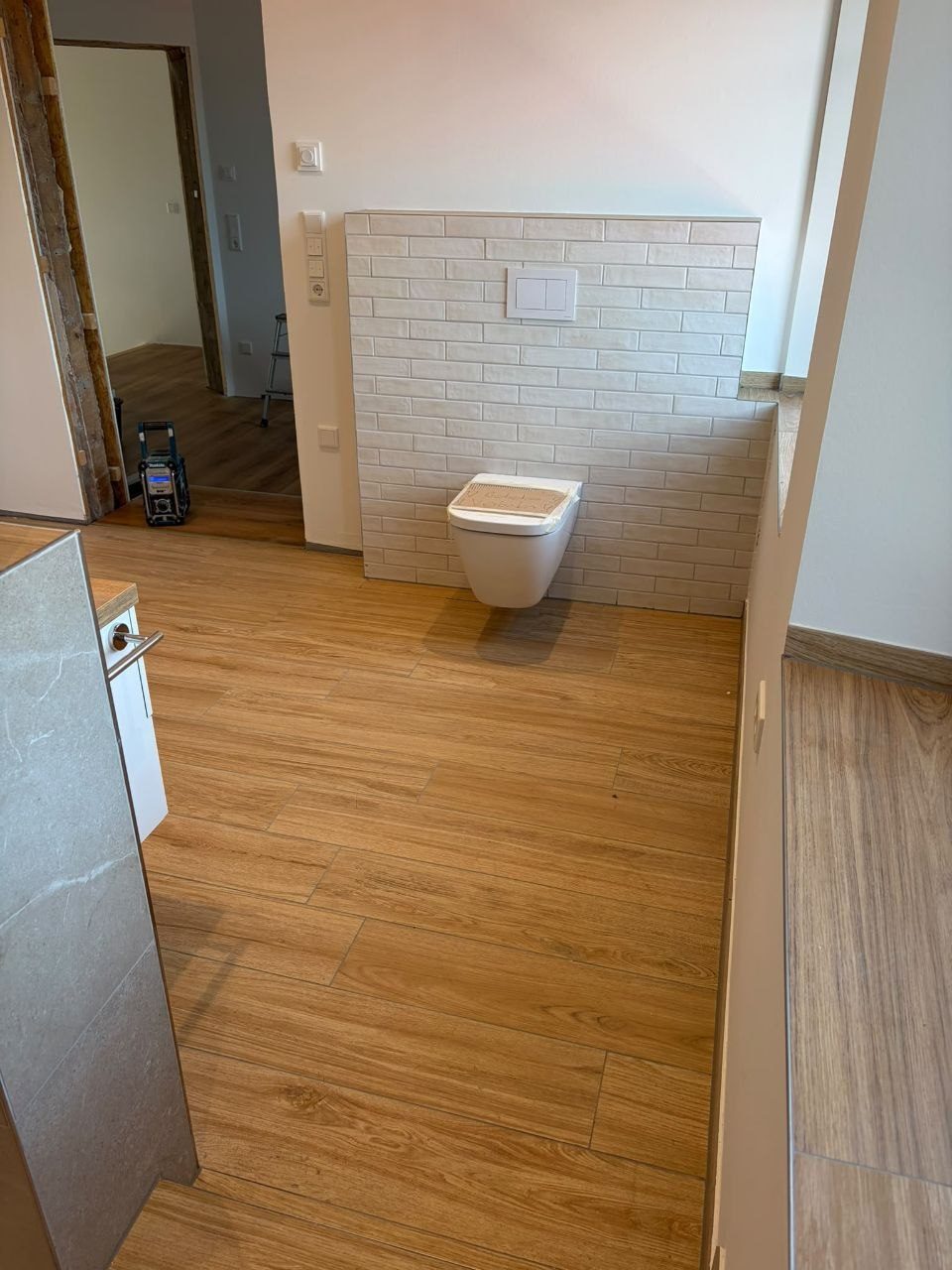 WC-Vorwand aus weißen Riemchen, davor der Holzoptik-Boden im wilden Verband