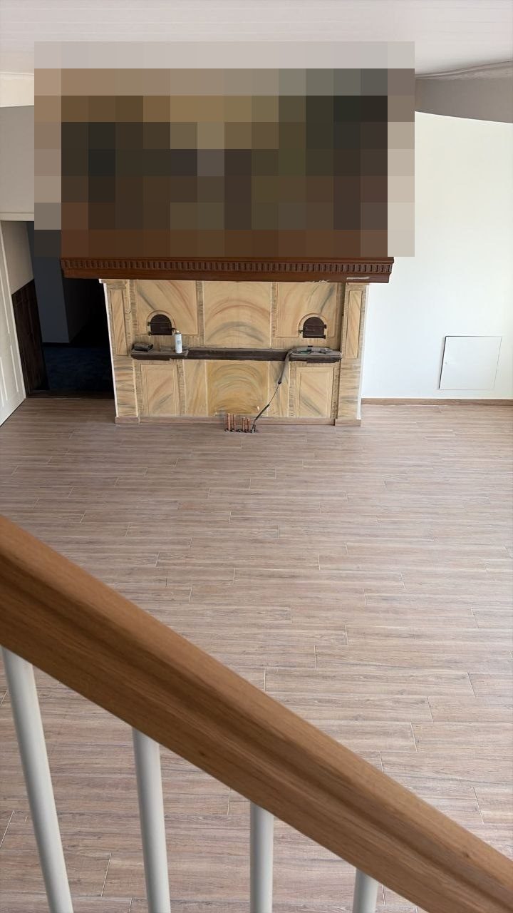 Kaminzimmer derselben Baustelle mit frisch verlegtem Holzoptik-Boden, das Gemälde über dem Kamin ist aus Urheberrechtsgründen unkenntlich gemacht